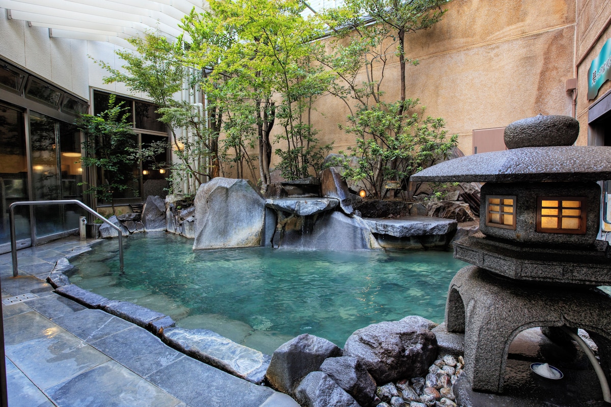 Outdoor bath with rocks, plants and a stone lantern at Hotel Shiragiku