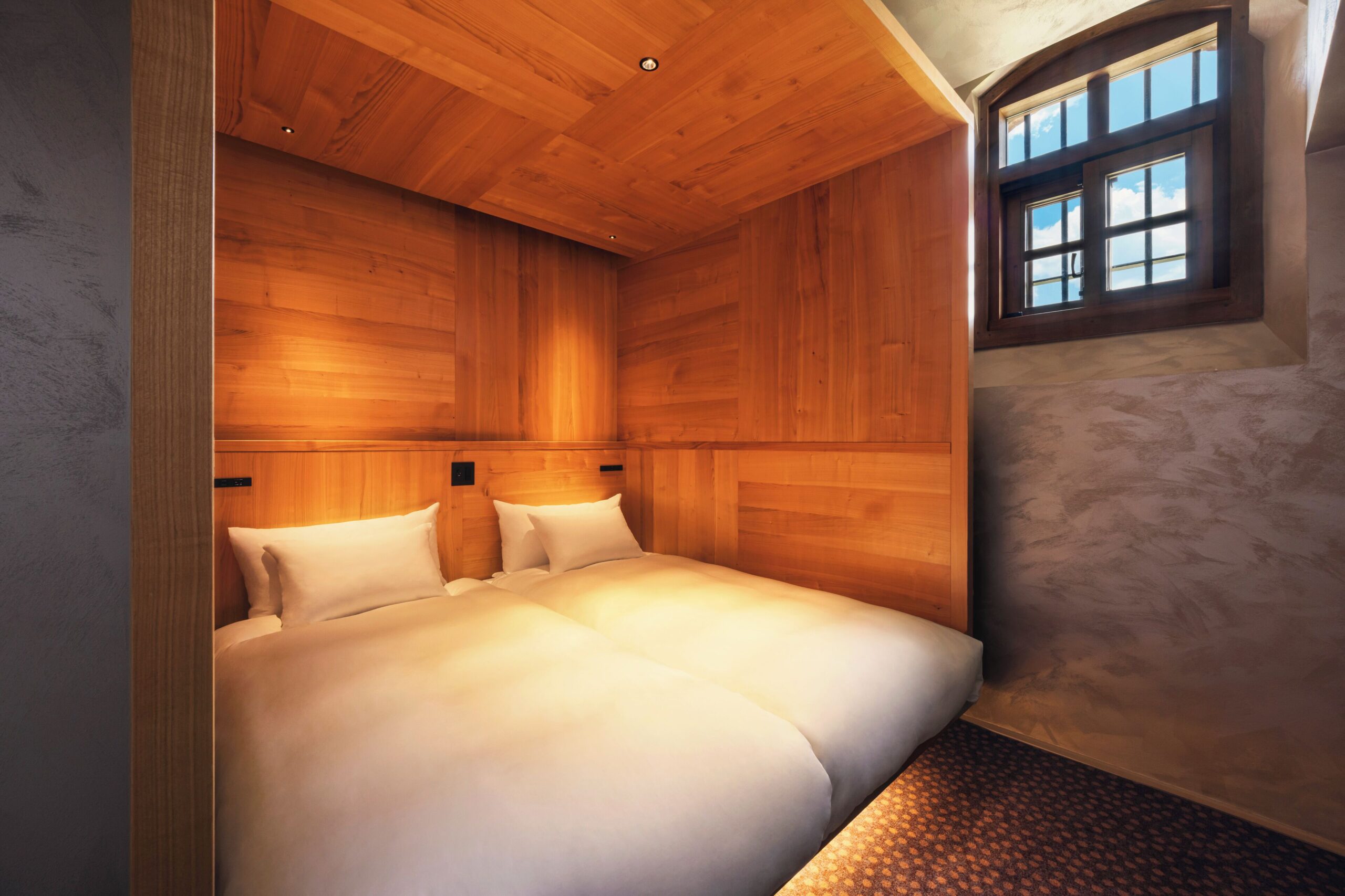 Two beds set side by side beneath wood paneling in a suite at HOSHINOYA Nara Prison